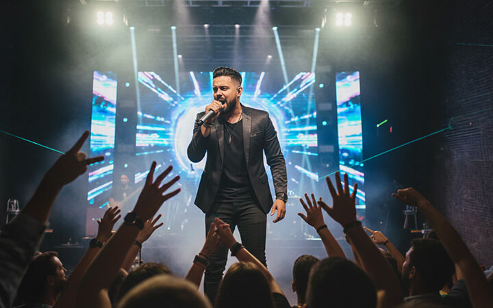 Felipe Lucas em show com banda completa, palco iluminado e público com as mãos levantadas